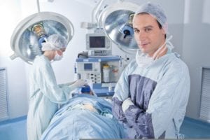 smiling male doctor with arms crossed in operating room